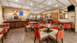 A hotel dining area with multiple tables and chairs, a kitchen area, and a television mounted on the wall. - Comfort Inn Valentine (Valentine)