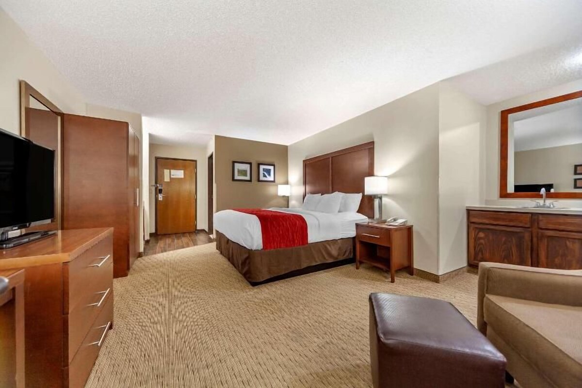 A hotel room with a bed, a desk, a TV, a mirror, and a bathroom.