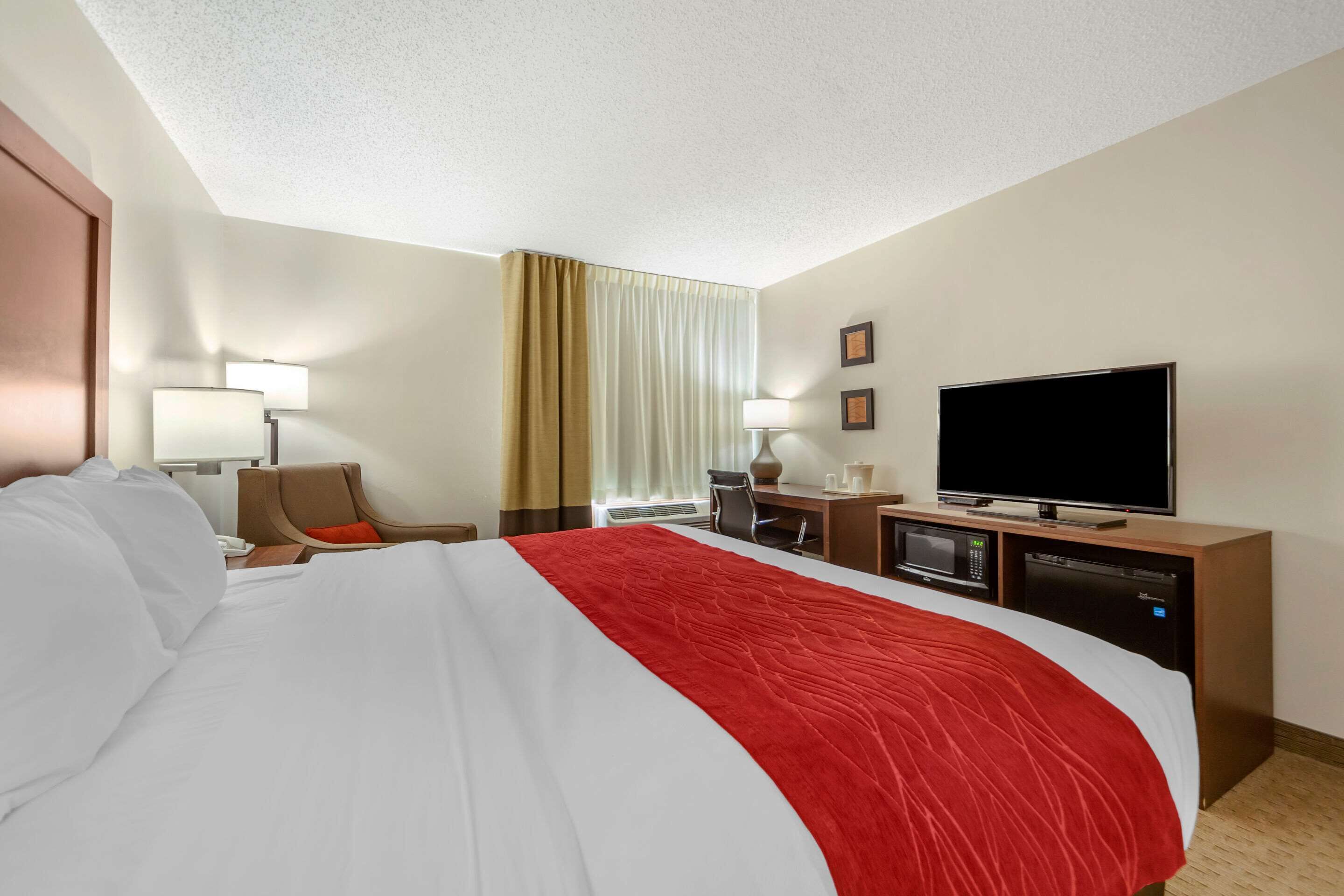 A hotel room with a large bed, a desk with a computer, a flat-screen TV, and a microwave.