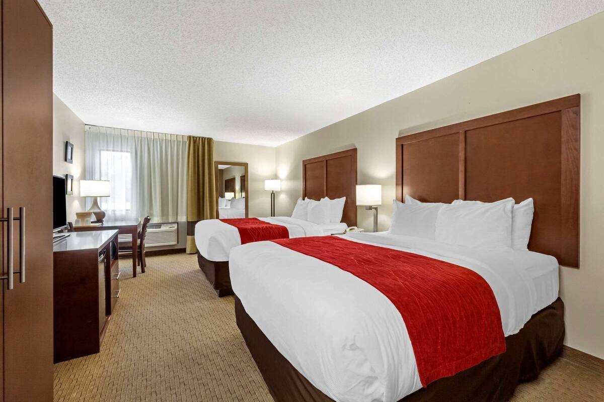 A hotel room with two beds, a desk, and a chair.
