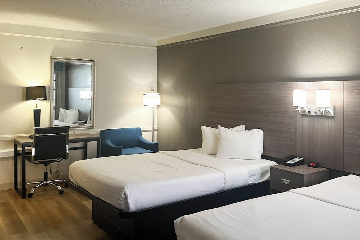 A hotel room with two beds, a desk, a chair, a mirror, a lamp, and a phone on the nightstand.