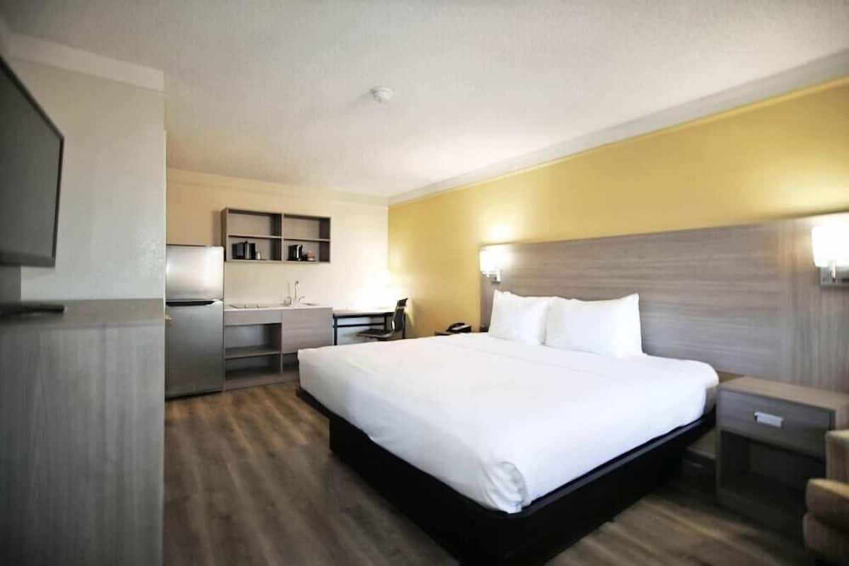 A hotel room with a bed, bedside table, lamp, desk, and a small kitchenette.