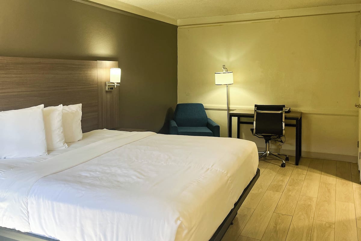 A hotel room with a large bed, a desk, a chair, and a lamp.