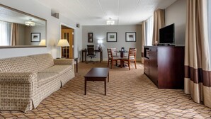A hotel room with a sofa, a dining table with chairs, a TV, a desk with a chair, and framed pictures on the wall. - Comfort Inn & Suites Glen Mills - West Chester (Glen Mills)