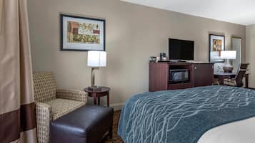 A hotel room with a bed, a sofa, a chair, a small table with a lamp, a TV, and a microwave.