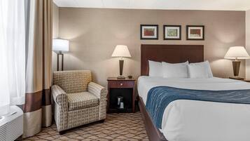 Una habitación de hotel con una cama, dos mesitas de noche con lámparas, un sillón estampado y una pared con tres cuadros enmarcados.