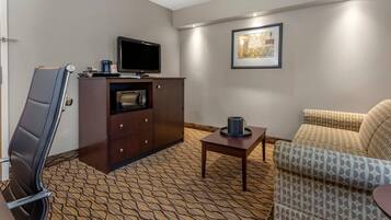 A hotel room with a sofa, a television on a cabinet, a patterned carpet, and a framed picture on the wall.