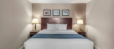 A hotel room with a large bed, two bedside tables, a headboard, and three framed pictures on the wall.