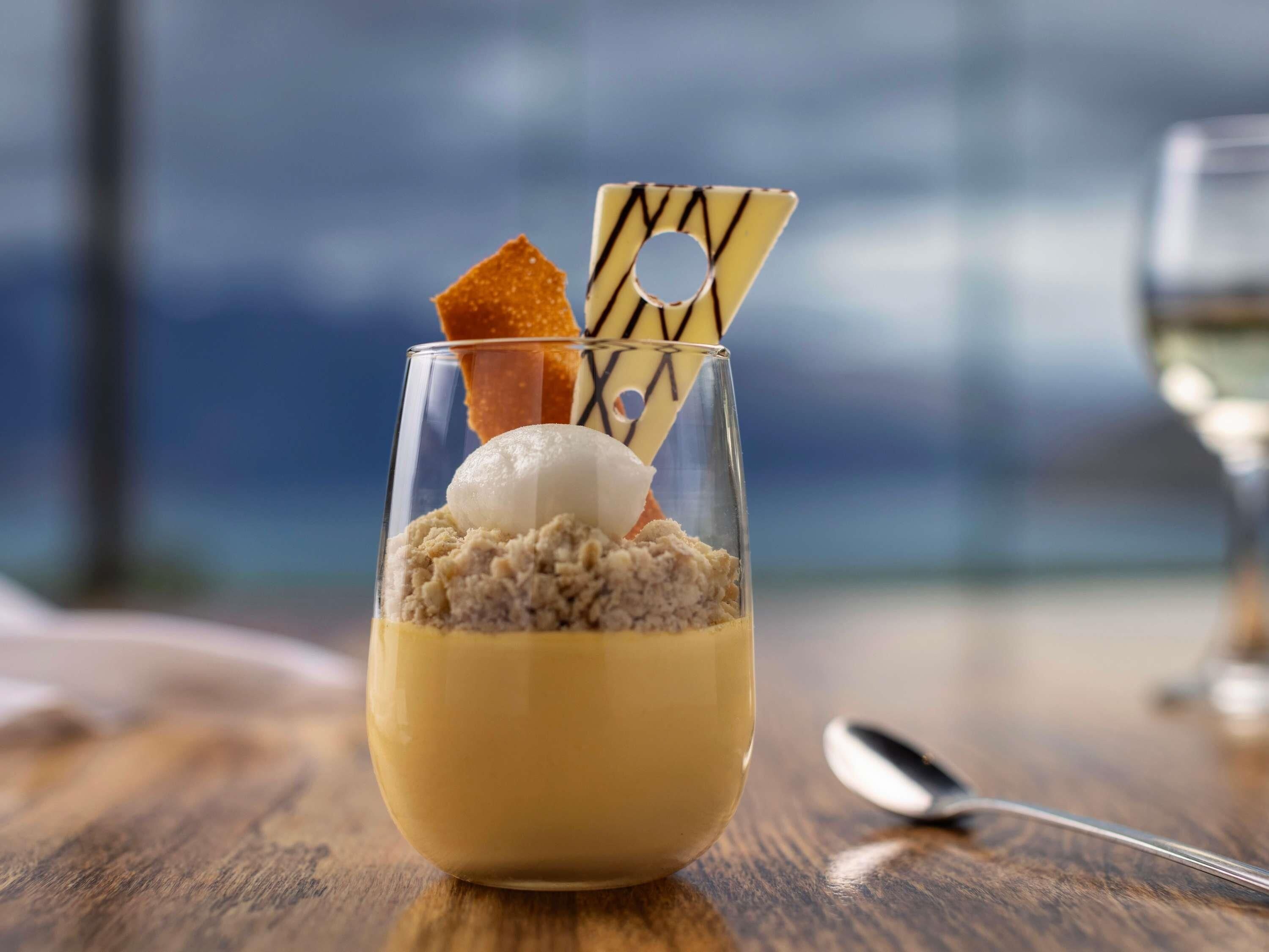 Un postre en una copa de vidrio transparente con una cuchara al lado.