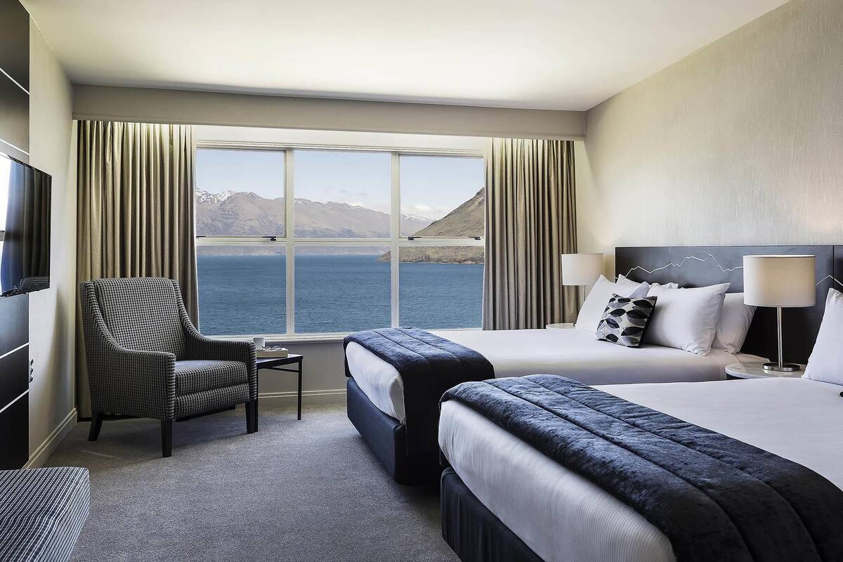 Ein Hotelzimmer mit großem Fenster, einem Bett, einem Sessel, einem Fernseher und einer Lampe.