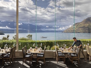 A restaurant with a view of a lake and mountains, with a waiter attending to a table. - Mövenpick Queenstown (Queenstown)