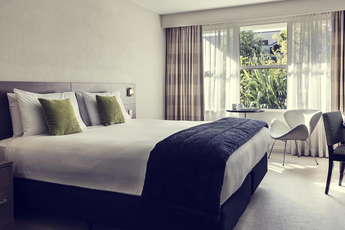 Une chambre d’hôtel avec un grand lit, un bureau, une chaise et une fenêtre avec des rideaux.