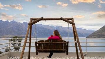 A wooden swing set with a person sitting on it, overlooking a lake with mountains in the background.
