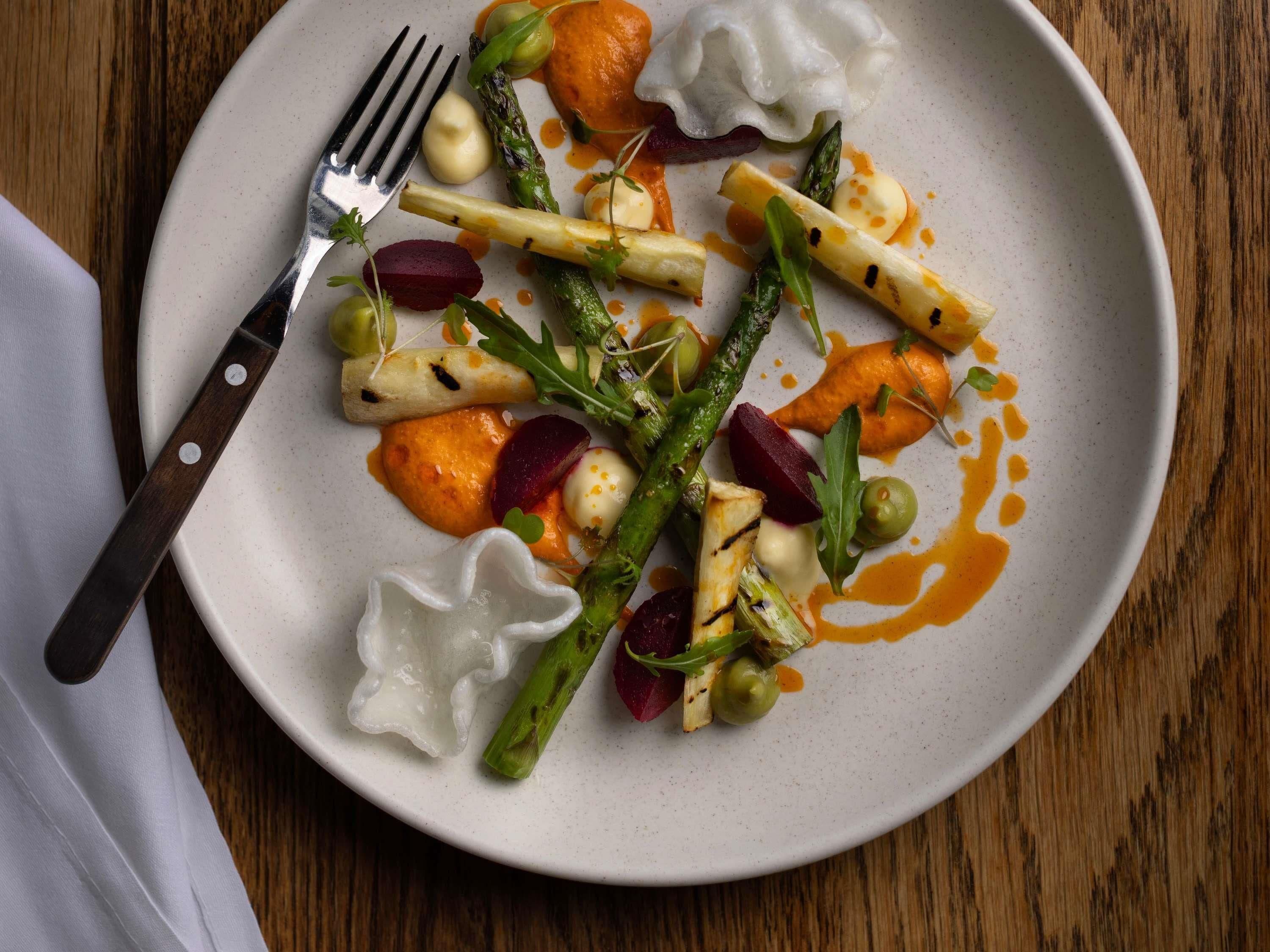 A plate of food with various vegetables and a white sauce, accompanied by a fork on a wooden table.
