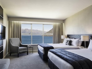Una habitación de hotel con un ventanal grande, una cama, una silla, un televisor y una lámpara.
