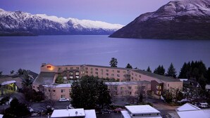 A hotel with a large building, a parking lot, and a view of snow-capped mountains and a lake. - Mercure Queenstown Resort (Queenstown)