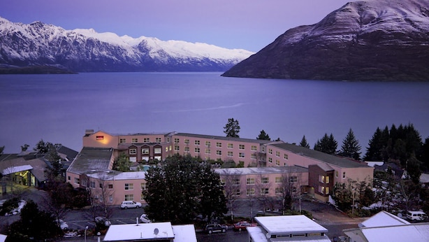 A hotel with a large building, a parking lot, and a view of snow-capped mountains and a lake. - Mercure Queenstown Resort (Queenstown)