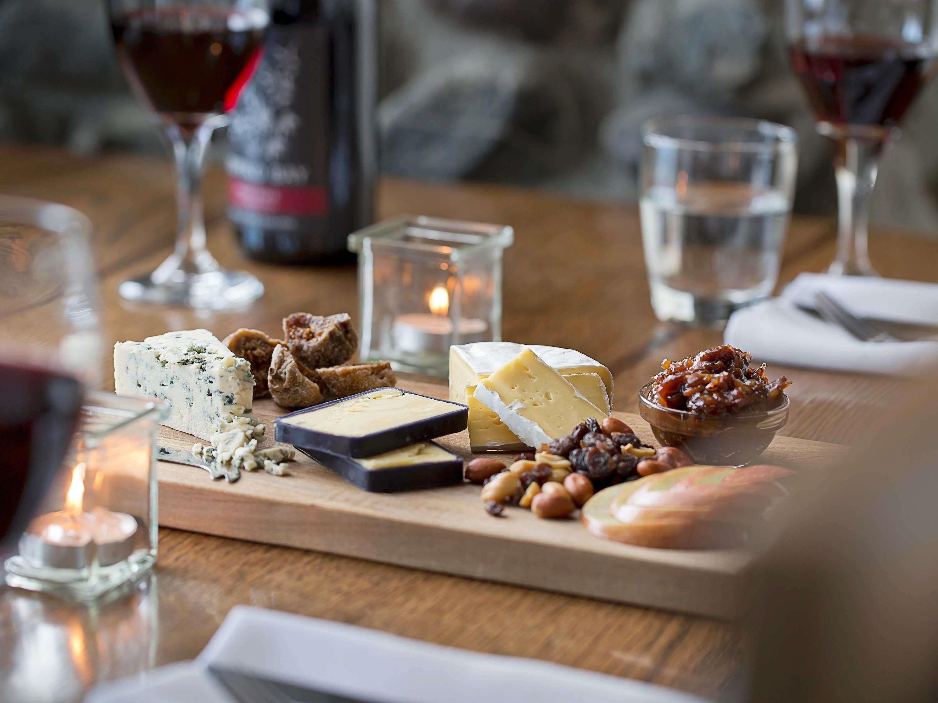 Een houten plank met diverse kazen, noten en een schaal gedroogd fruit op een tafel.