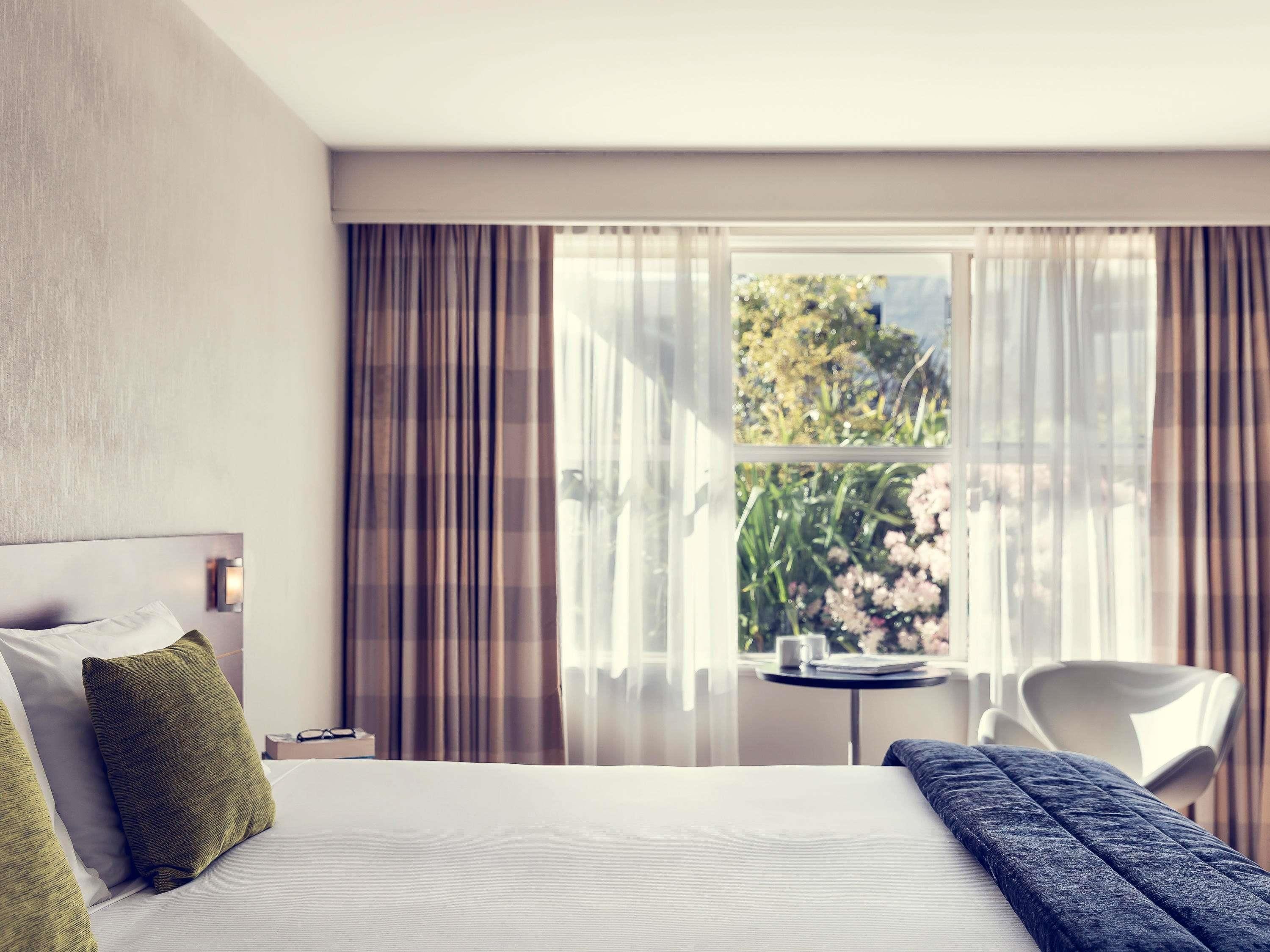 Une chambre d’hôtel avec un lit, une petite table, une chaise et une fenêtre avec des rideaux.