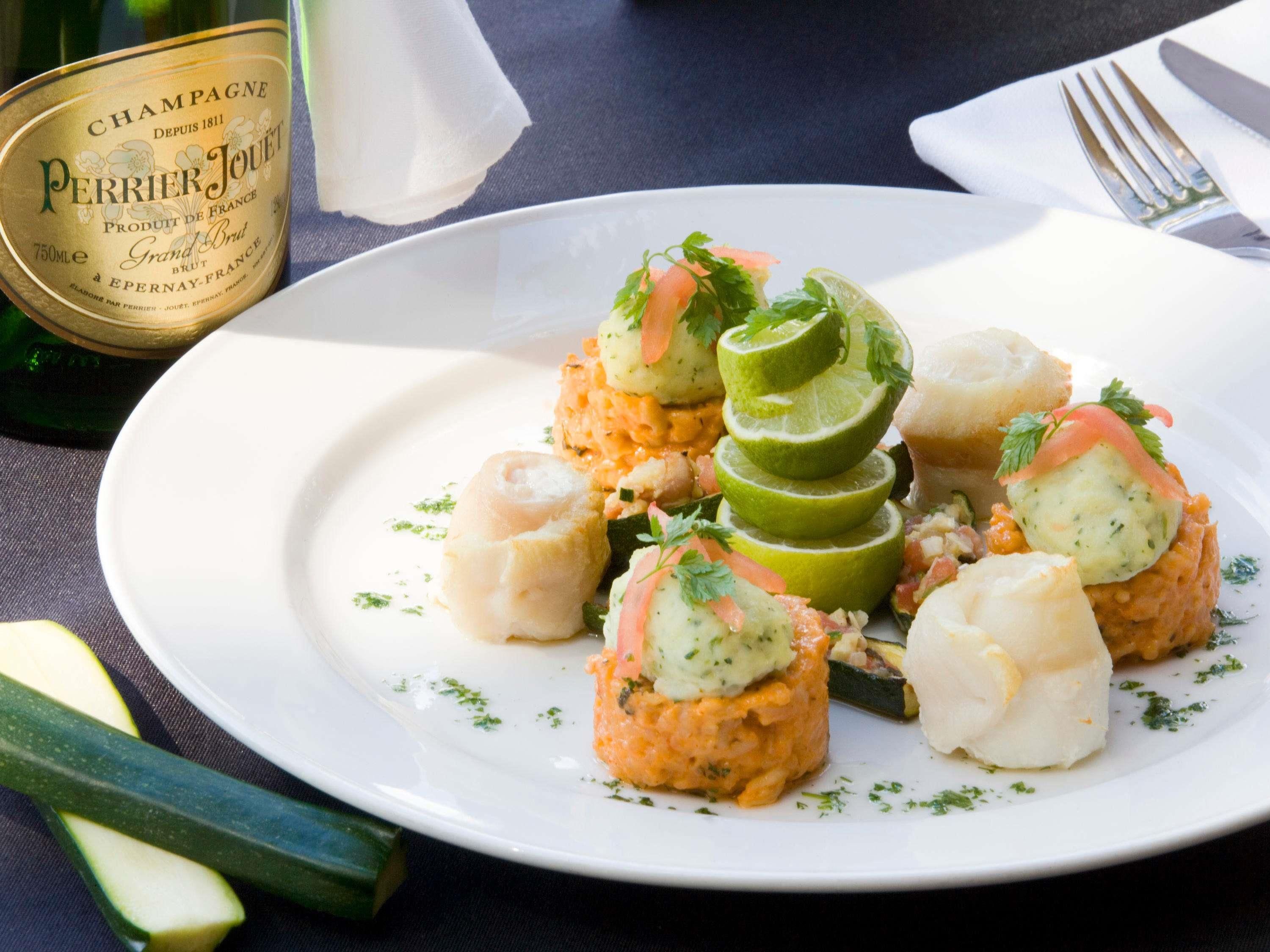 A plate of food with a bottle of Perrier Jouet champagne in the background.