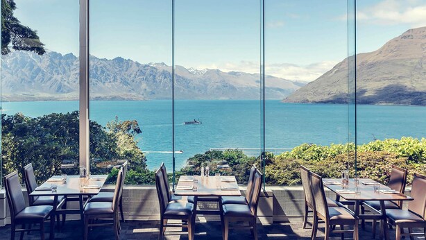 A restaurant with outdoor seating overlooking a lake and mountains. - Mercure Queenstown Resort (Queenstown)