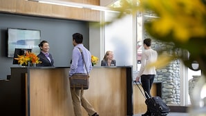 A reception desk with a digital screen, wooden paneling, and a stone wall. - Mercure Queenstown Resort (Queenstown)