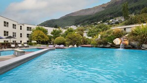 A swimming pool with a waterfall feature, surrounded by lush greenery and a mountain backdrop. - Mercure Queenstown Resort (Queenstown)
