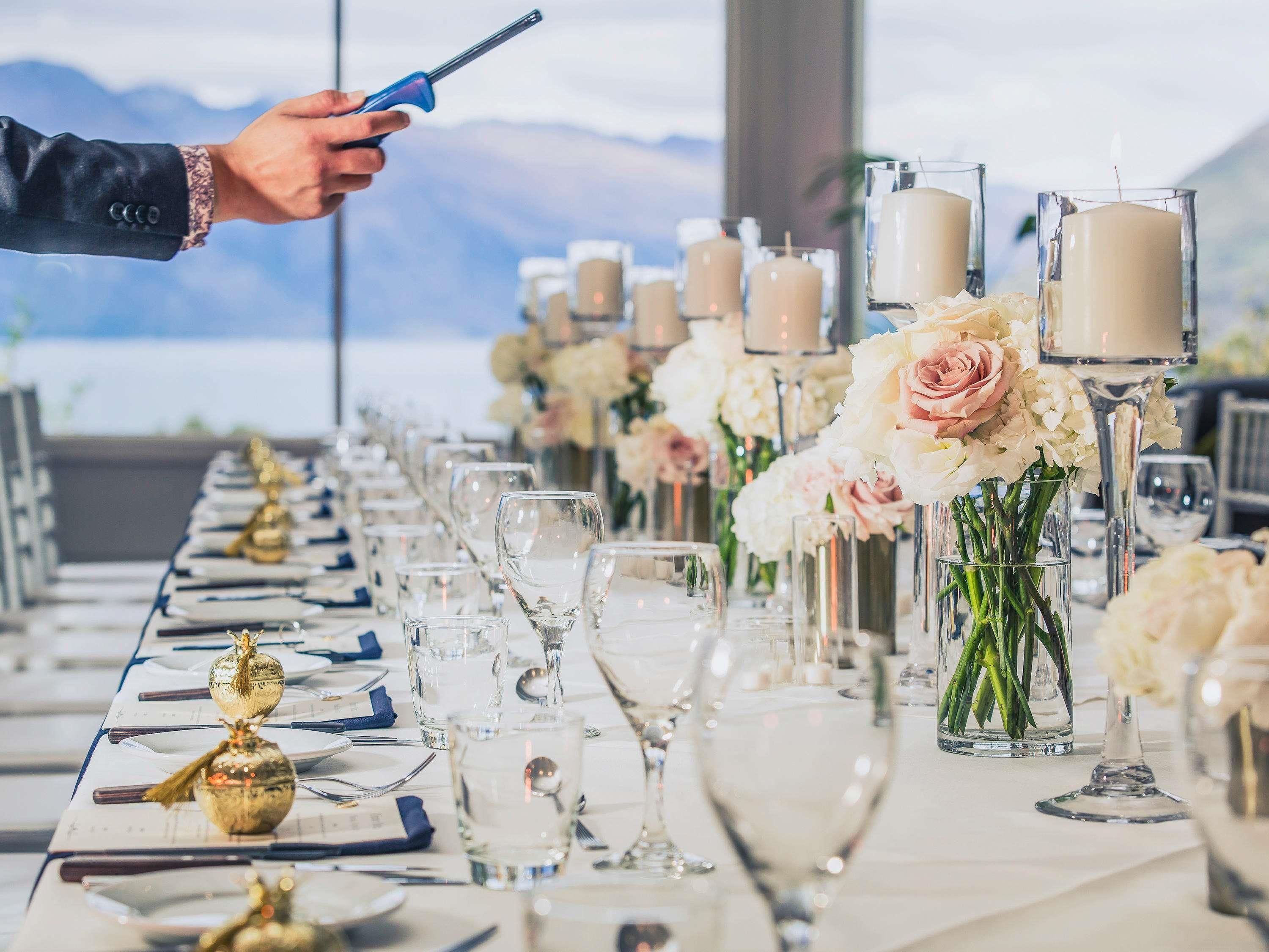 Mesa posta para um evento formal, com copos transparentes, velas e arranjos florais.