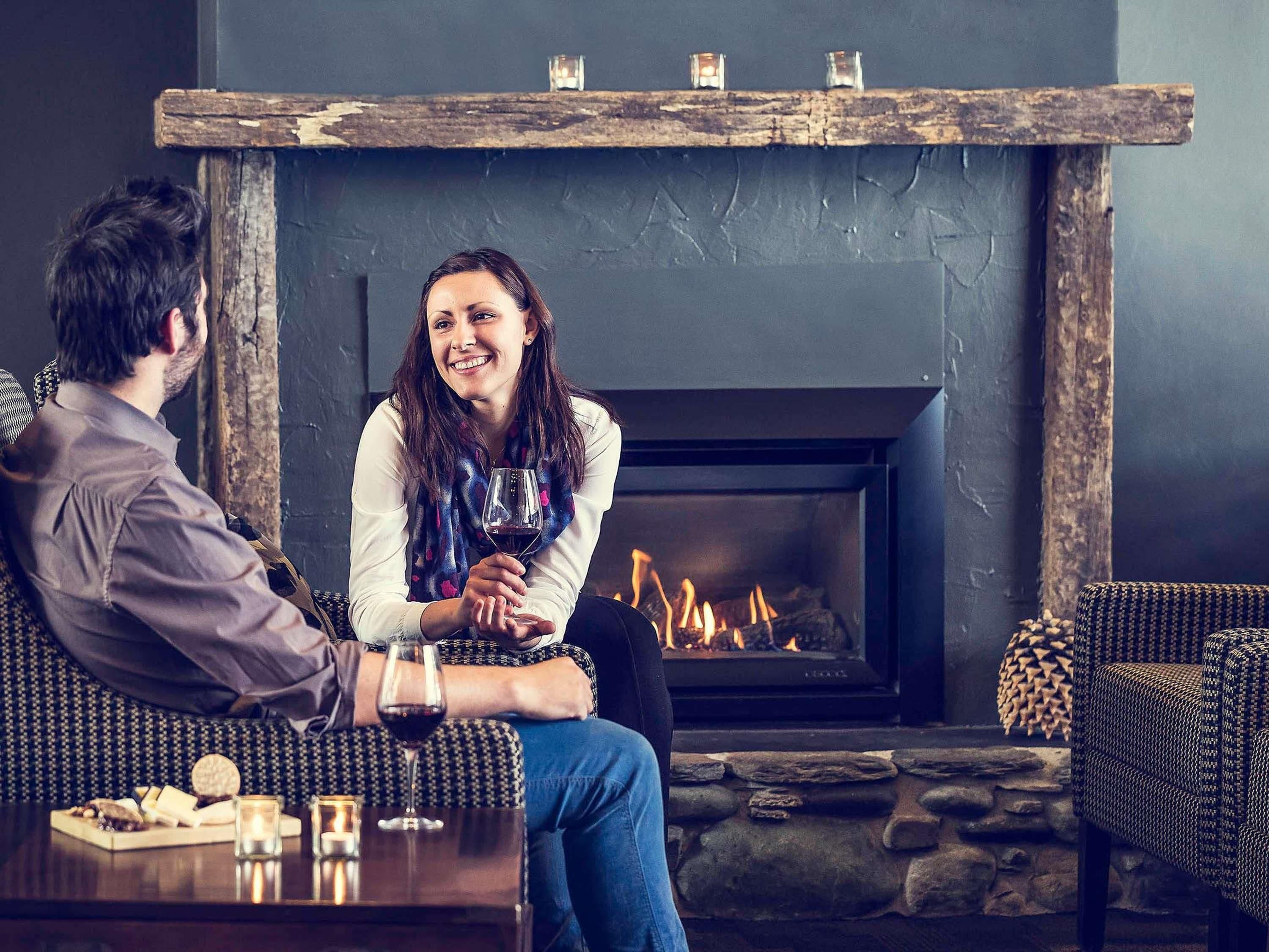 Ein Paar sitzt in einem gemütlichen Raum mit Kamin, einem Tisch mit Snacks und Getränken sowie einer Steinwand.
