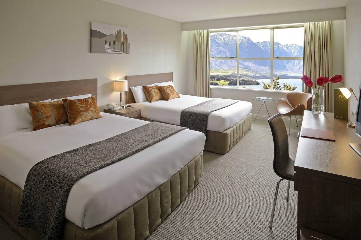 Ein Hotelzimmer mit zwei Betten, einem Schreibtisch, einem Stuhl, Bergblick und einem Bild an der Wand.