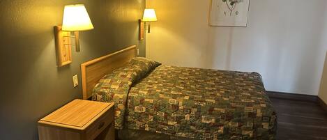 Un dormitorio con una cama de madera, dos lámparas de noche, una mesita de noche y una obra de arte floral enmarcada en la pared.