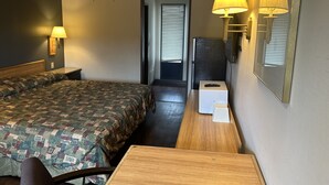 A hotel room with a large bed, a wooden desk, a chair, two wall-mounted lamps, and a refrigerator.