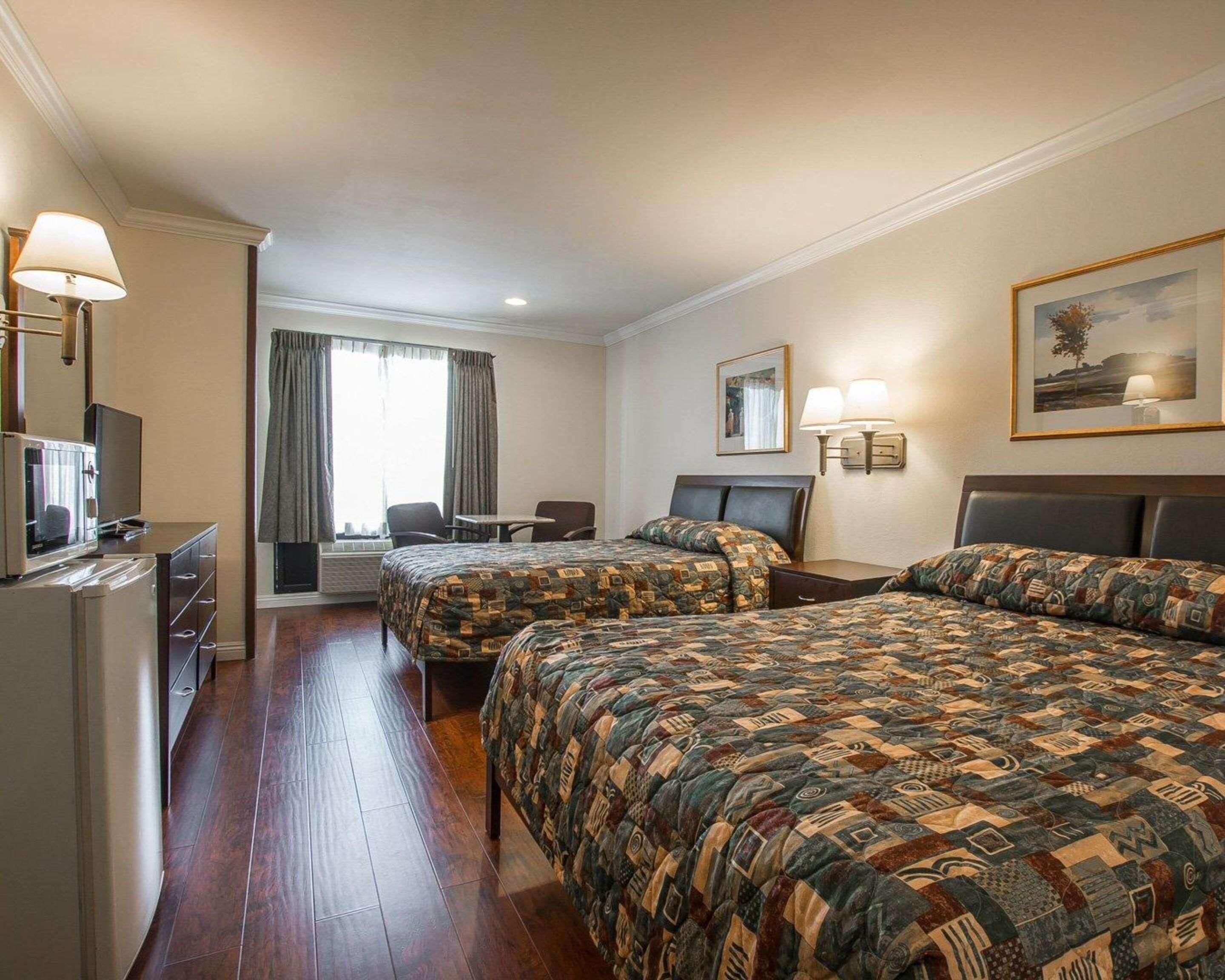 A hotel room with two beds, a desk, a chair, a TV, and a painting on the wall.