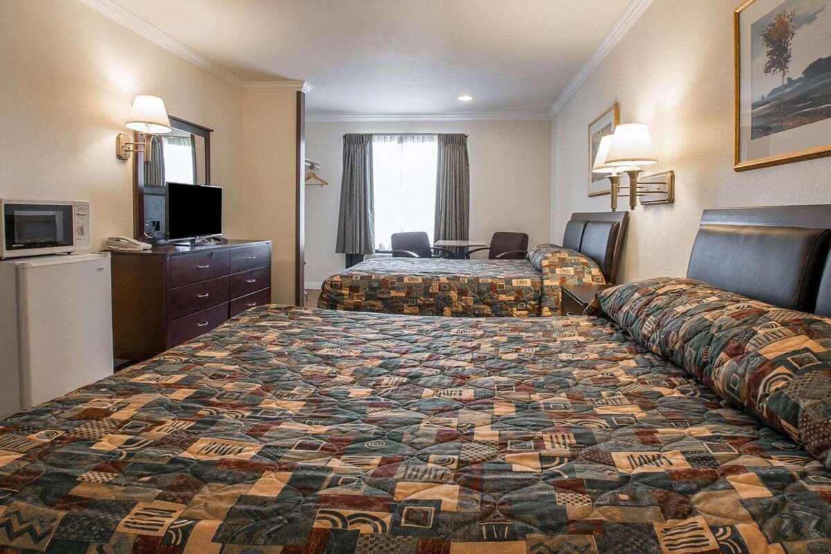 A hotel room with a large bed, a desk, a chair, a television, and a refrigerator.