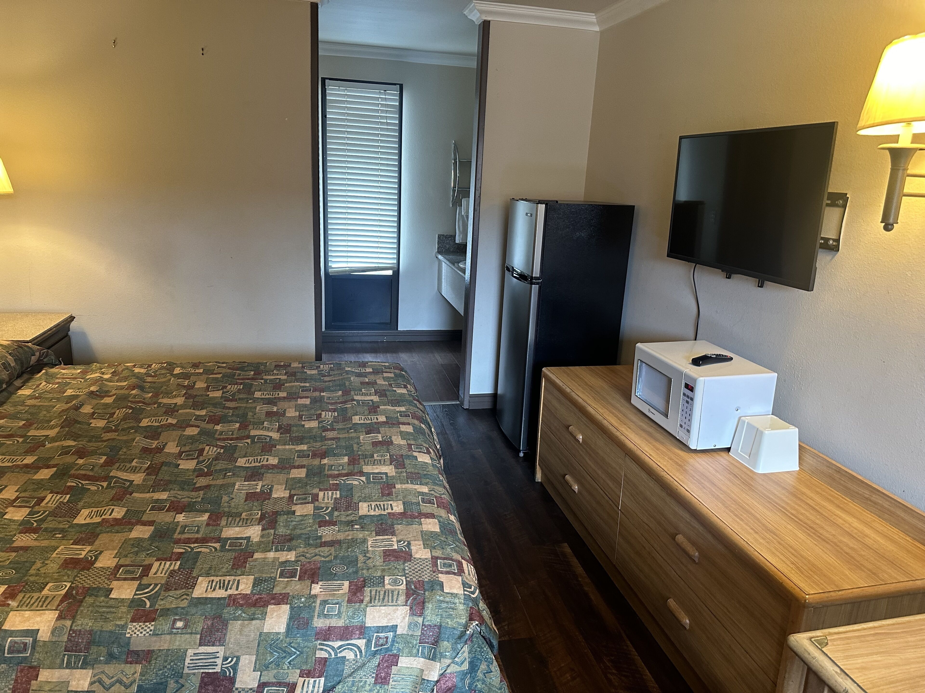 A hotel room with a bed, a dresser, a television, and a refrigerator.