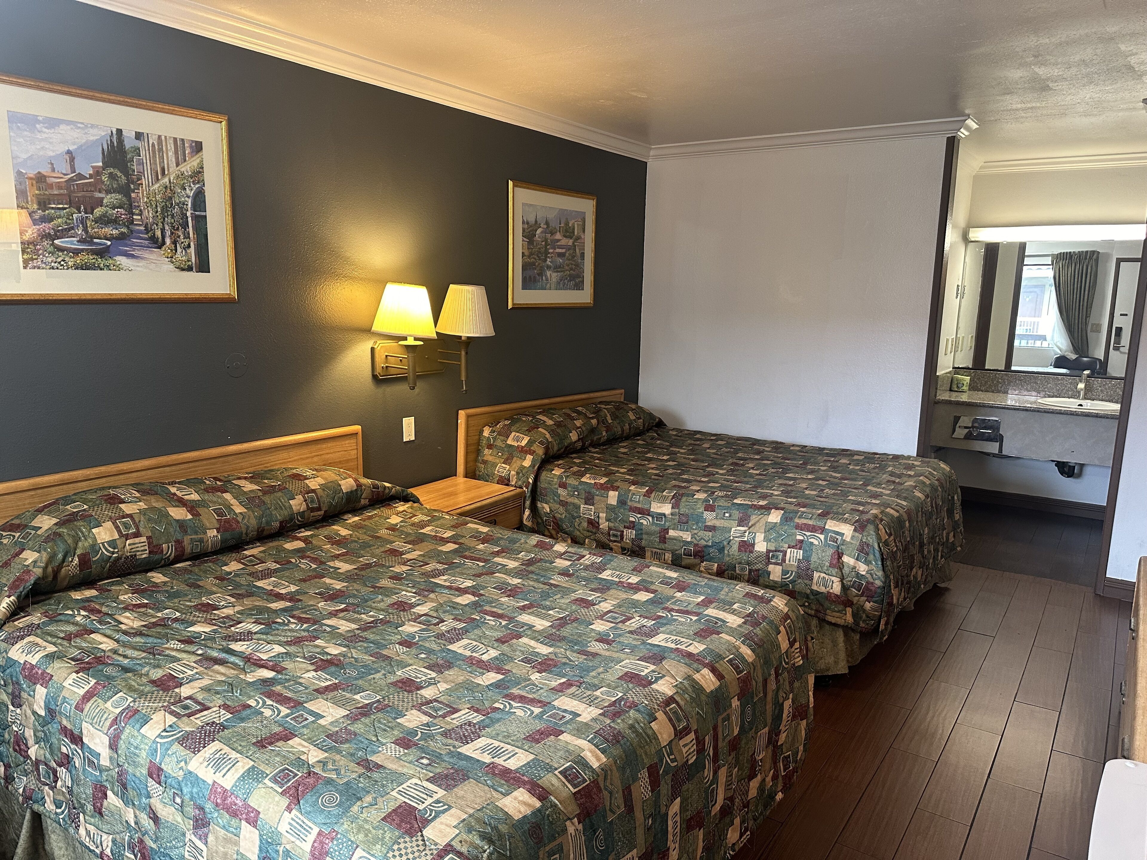Quarto de hotel com duas camas, uma mesa de cabeceira, uma luminária e um espelho.