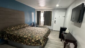 A hotel room with a large bed, a desk, a chair, a TV, and a door.