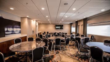 A conference room with multiple tables and chairs, a mounted TV, and a large window with a view.