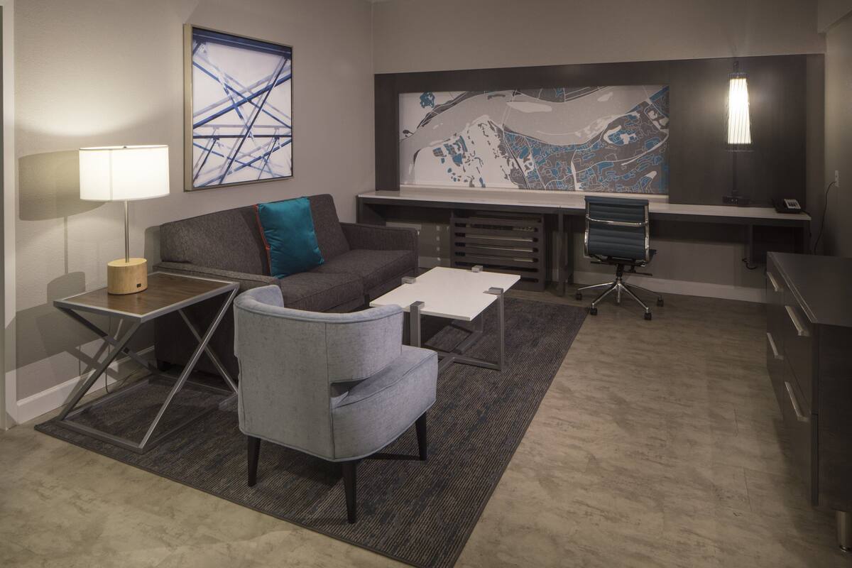 A modern office space with a grey sofa, a small armchair, a desk with a lamp, and a large map on the wall.