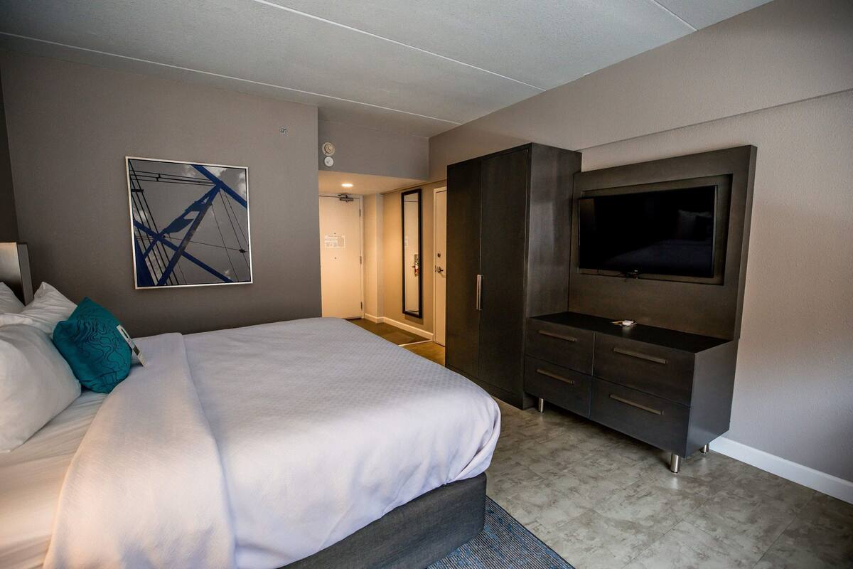 A modern bedroom with a large bed, a TV mounted on the wall, and a walk-in closet.
