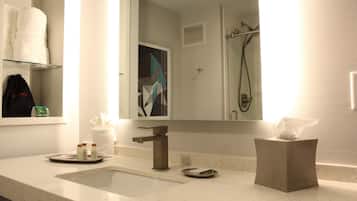 A hotel bathroom with a sink, mirror, towel rack, and shower area.