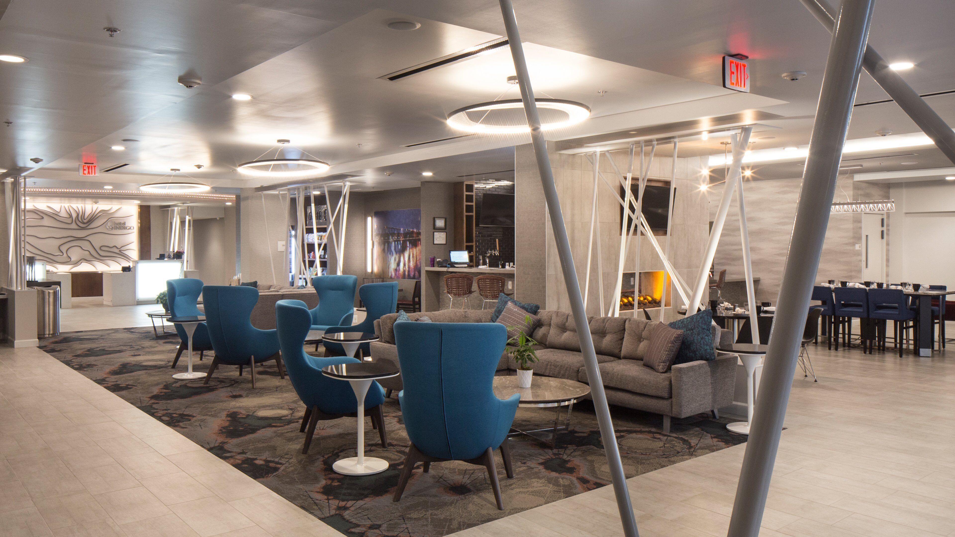 Um lobby de hotel moderno com poltronas azuis, um sofá, uma lareira e um balcão de recepção.
