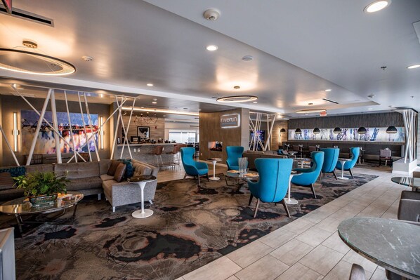 Un moderno vestíbulo de hotel con una zona de estar que incluye sofás y sillones, un área de bar y un amplio ventanal con vistas.