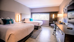 Una habitación de hotel moderna con dos camas, un escritorio, un televisor y un ventanal grande.