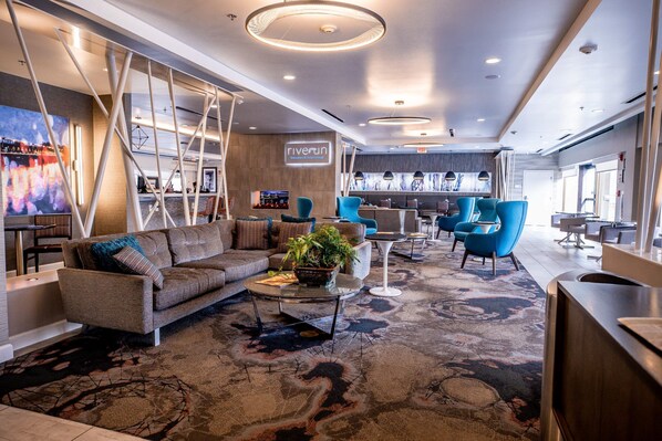A modern hotel lobby with a sofa, chairs, a coffee table, and a TV. - Hotel Indigo Harrisburg - Hershey by IHG (Harrisburg)