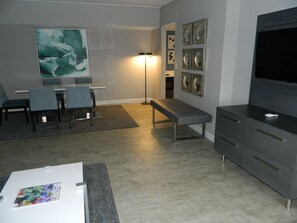 A modern living room with a dining area, a bench, a flat-screen TV, and artwork on the walls.