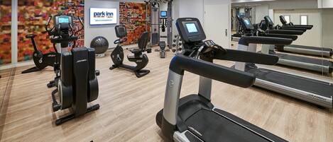 A modern gym with cardio machines, weights, and a mirrored wall.