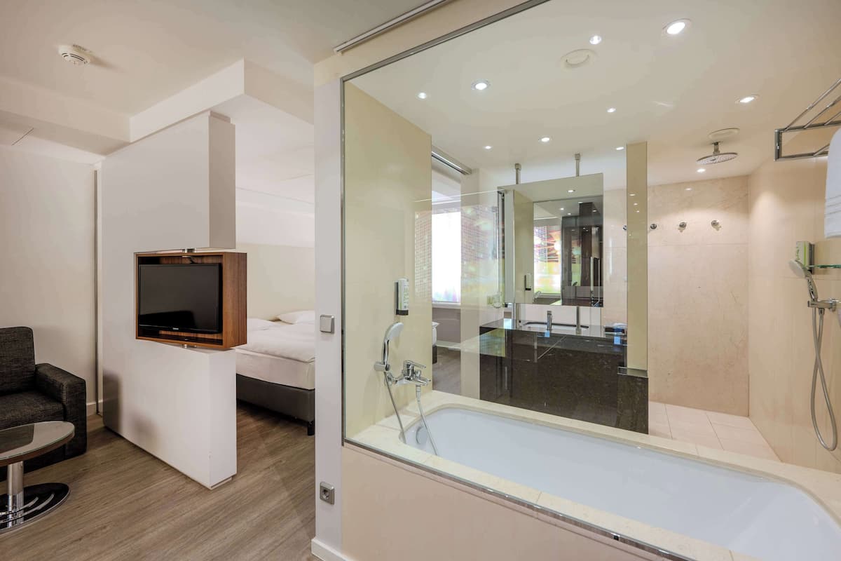 Una habitación de hotel moderna con una bañera grande, un televisor de pantalla plana, un sofá y una mesa de comedor.