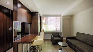 A modern living room with a wooden cabinet, a glass-top table, a leather chair, a grey sofa, and a small round table.