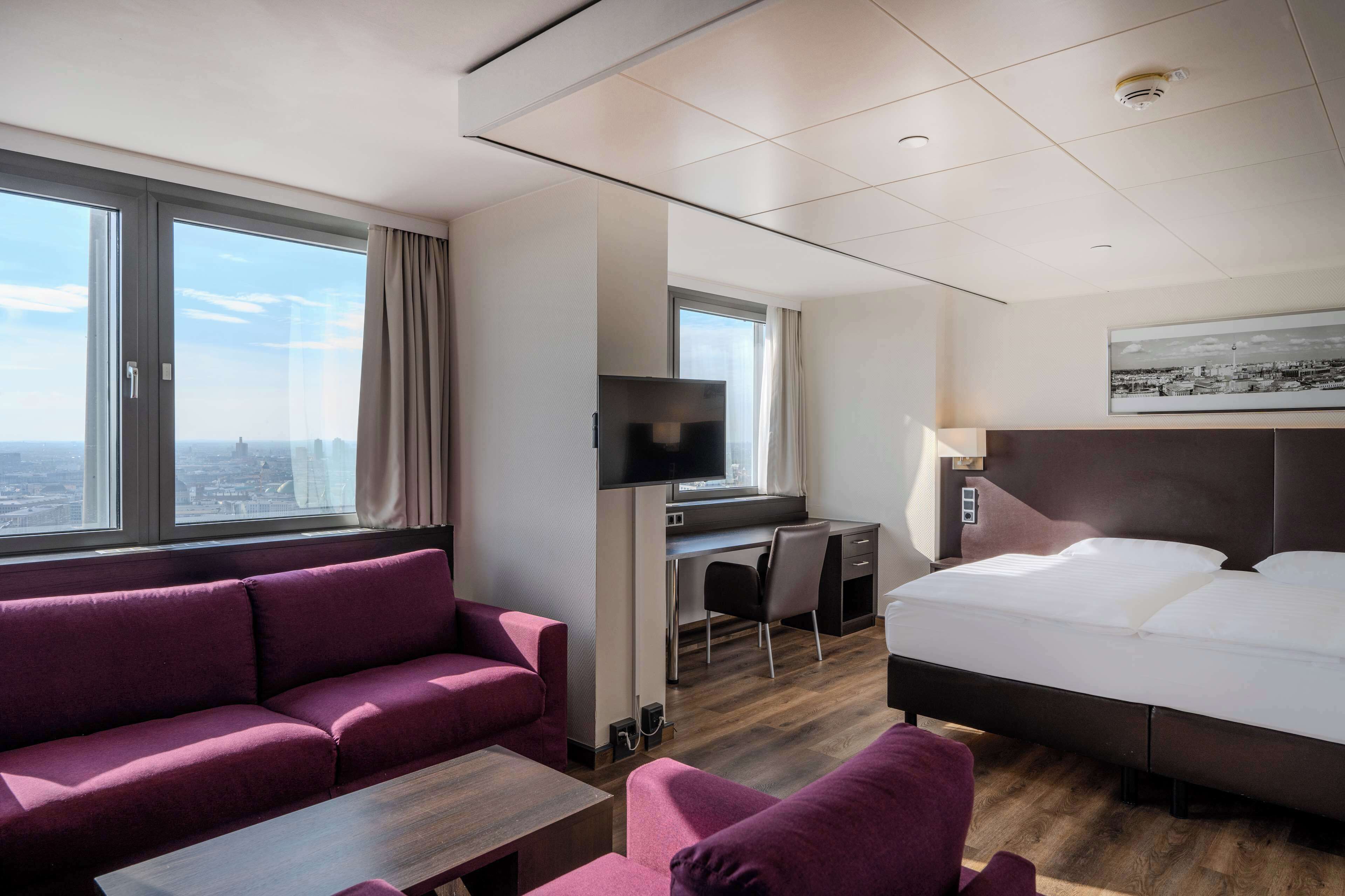 A hotel room with a large bed, a sofa, a desk, and a television.